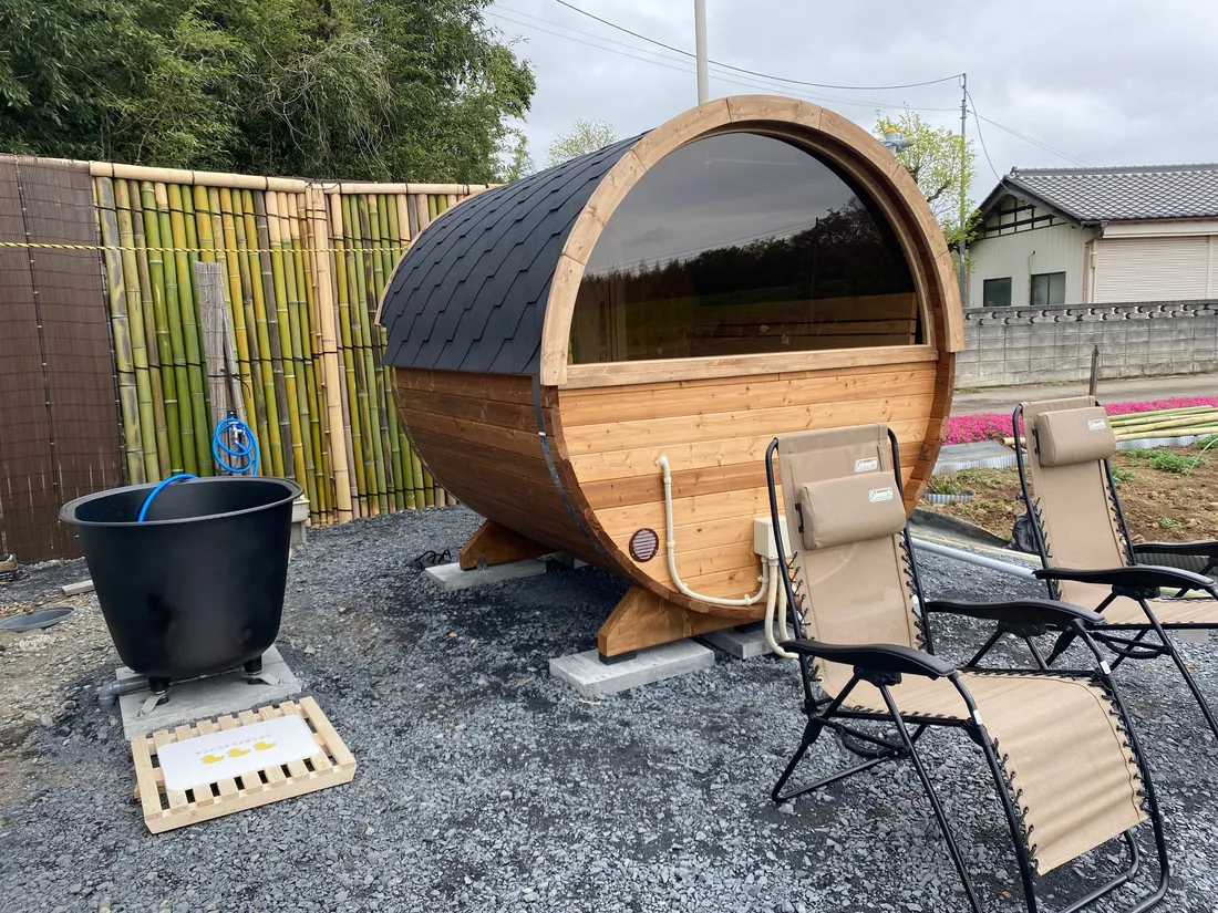 The completed Estonian barrel sauna outdoors with its cast-iron cold plunge tub and lounge chairs