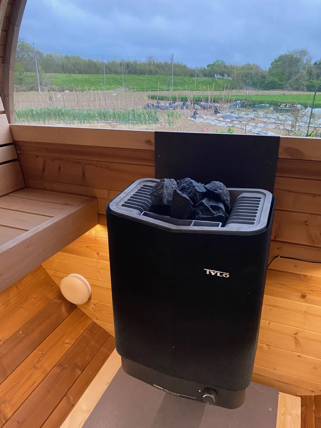 The Tylö heater and benches inside the barrel sauna, fields visible through the window